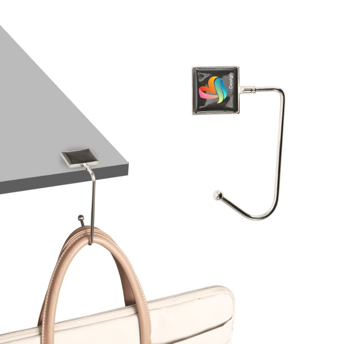 A square silver desk hook with a curved arm holding a handbag, set against a light background. It includes a logo.