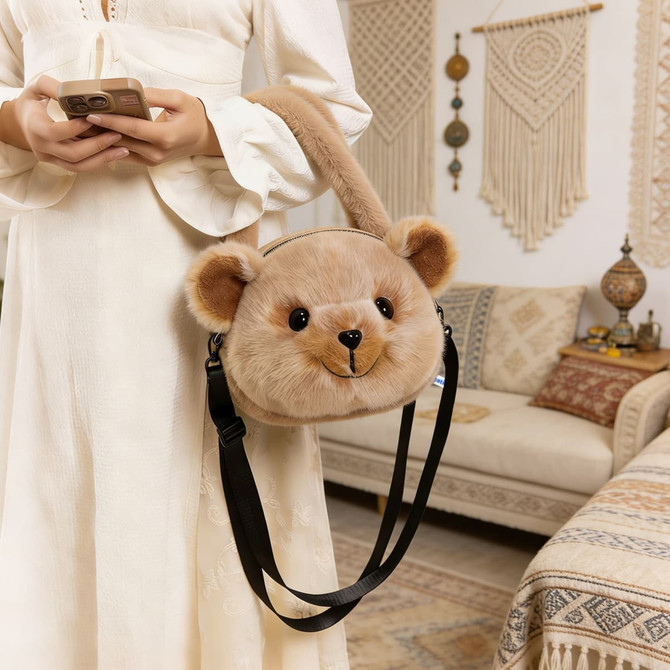 A plush handbag featuring a cute bear design in light brown, with a black strap, being held by a person.