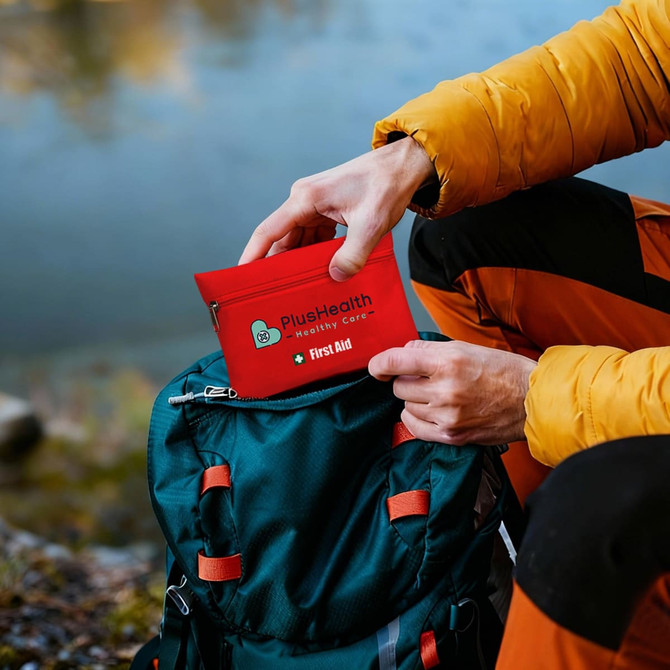 A bright red first aid kit pouch being taken from a green backpack near a lake. The pouch has a logo.