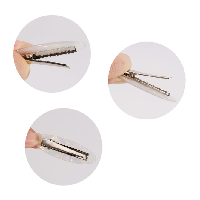 An oval iridescent alligator hair clip, showcasing its shiny surface and clip mechanism, held between fingers.