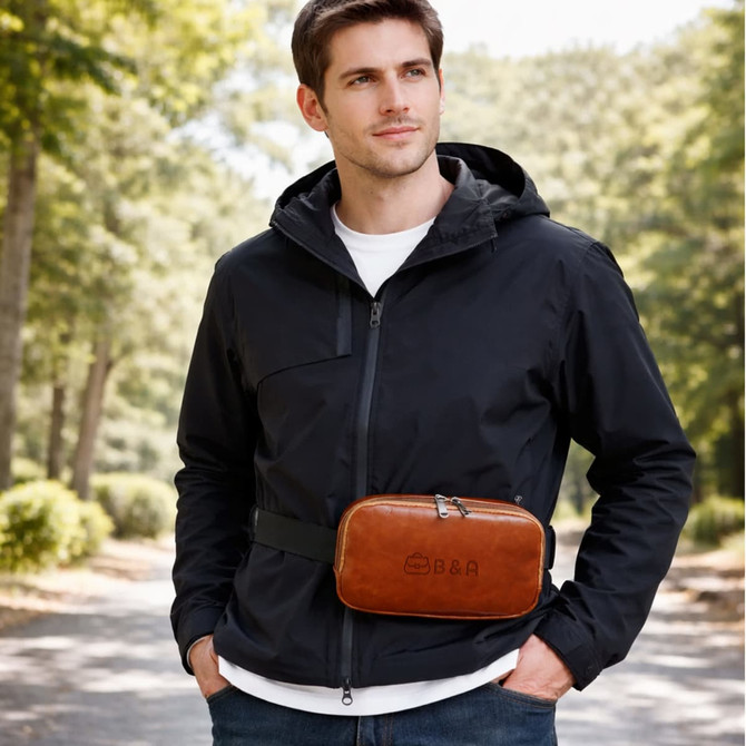 A man wearing a black jacket stands outdoors, featuring a brown polyurethane fanny pack with a logo.
