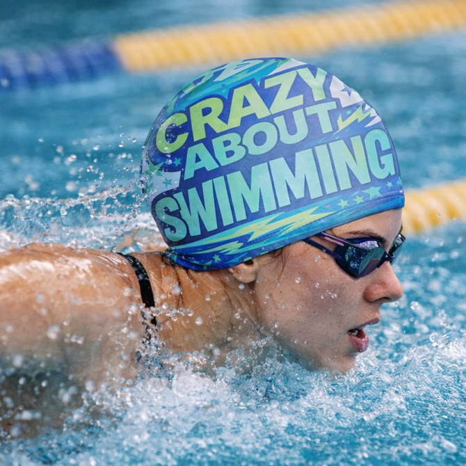 A full colour polyester swimming cap in blue and green with a logo, worn by a swimmer in the water.