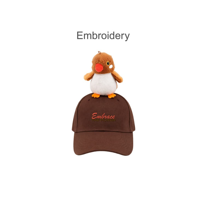 A brown baseball cap with a plush bird on top and decorated embroidery. The cap has a logo.