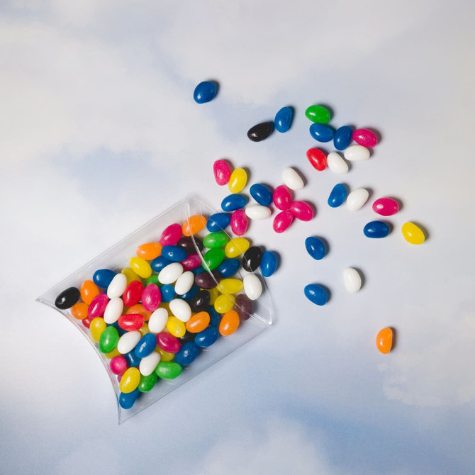 Assorted mini jelly beans in various colours, including black, white, blue, green, pink, orange, and yellow, in a pillow pack.