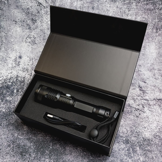 A black rechargeable torch with a charging cable, sitting inside a black box with cushioning.