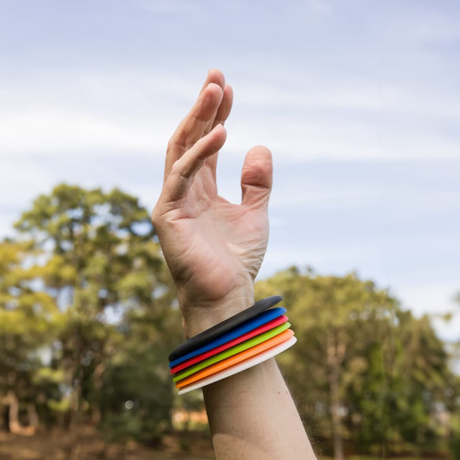 A hand wearing colorful silicone wristbands in blue, red, yellow, green, orange, and white against a natural background.