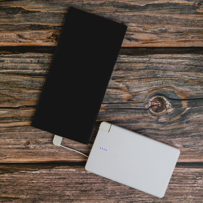 A white power bank with a sleek design, connected to a device, resting on a wooden surface.