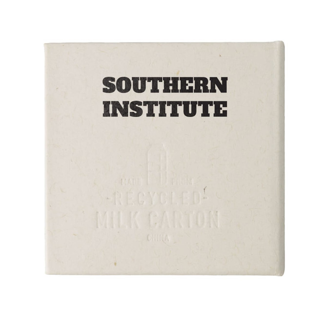 A square, off-white note block made from recycled materials, featuring a logo and embossed text.