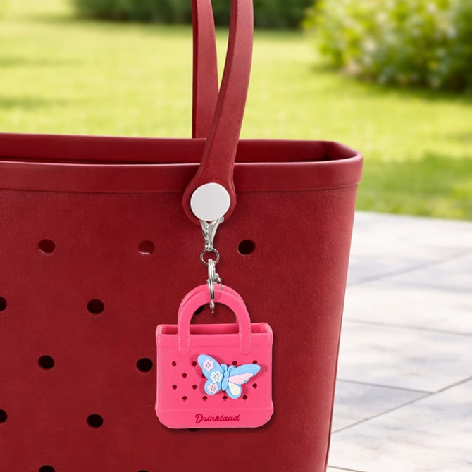 A pink Mini EVA holes bag keychain with a butterfly design hanging from a red tote bag.