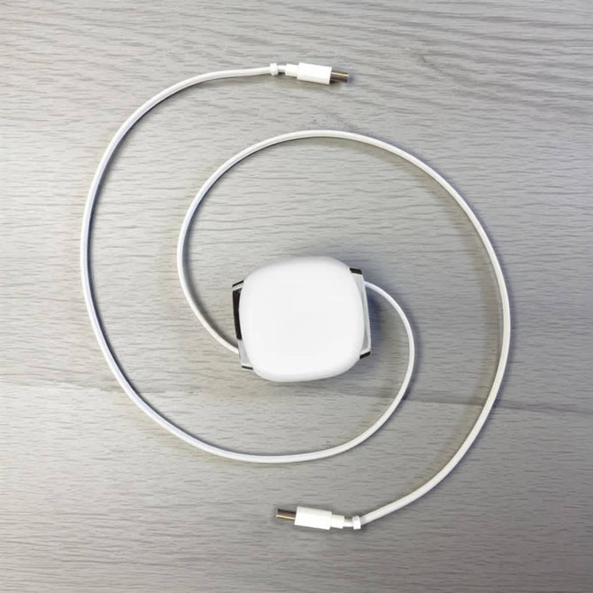 A retractable charging data cable in white, coiled with connectors at both ends, laid on a light wooden surface.