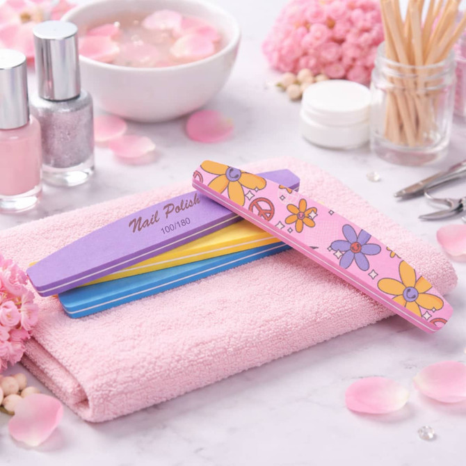 A sponge half-moon shaped nail file in purple, yellow, and pink, resting on a pink towel among beauty products and flowers.