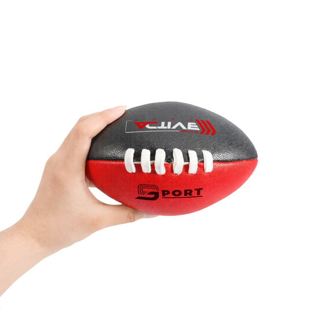 A hand holds a Mini Aussie Rules Ball, featuring black and red colours with white laces and a logo.