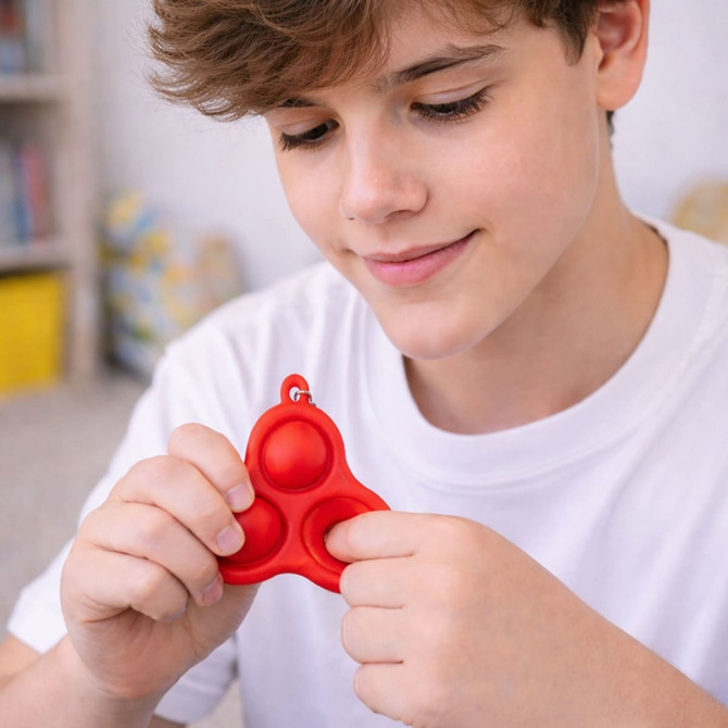 A red silicone keychain with three bubbles, held by a young person wearing a white shirt.