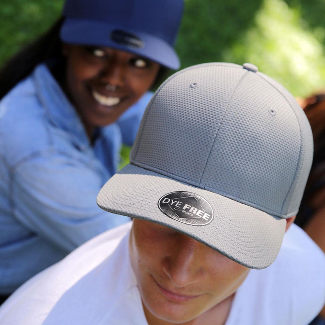 A grey cap with a textured surface and a logo, worn by a person, alongside a person in a navy cap.