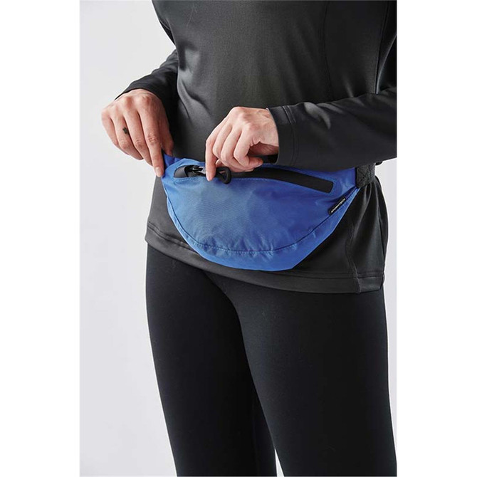 A blue Teton Waist Pack is being worn around the waist, featuring a secure zipper closure.
