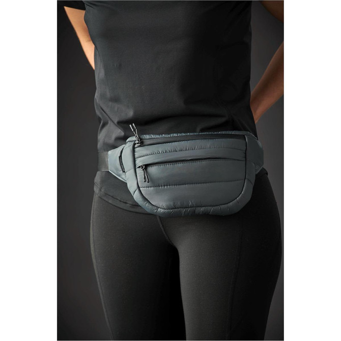A quilted waist bag in dark green worn around the waist by a person in black activewear. It features a logo.