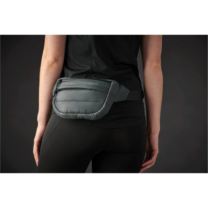 A quilted grey waist bag with a black adjustable strap worn at the waist. The bag features a zipper and a logo.