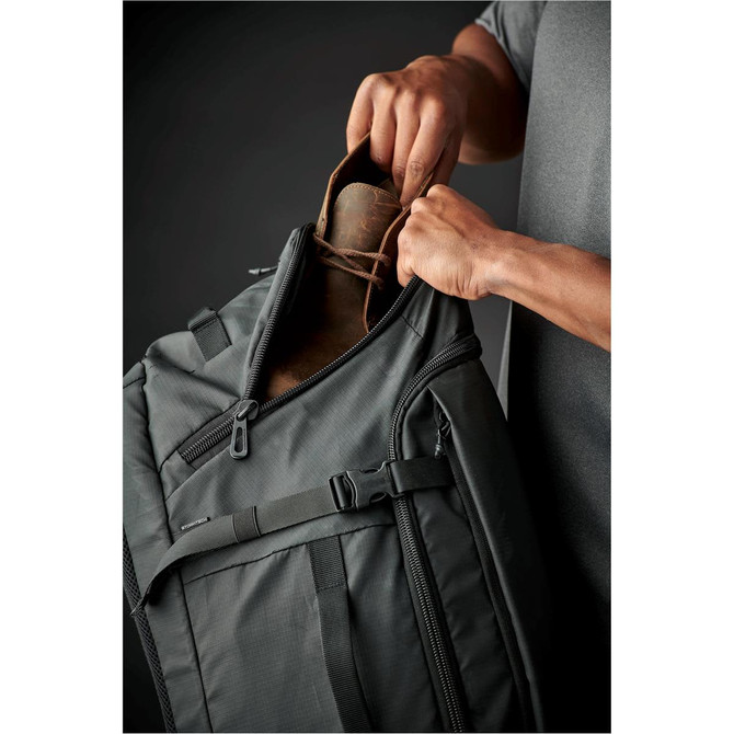 A dark green duffle bag being opened, with hands pulling out a brown drink bottle from inside.