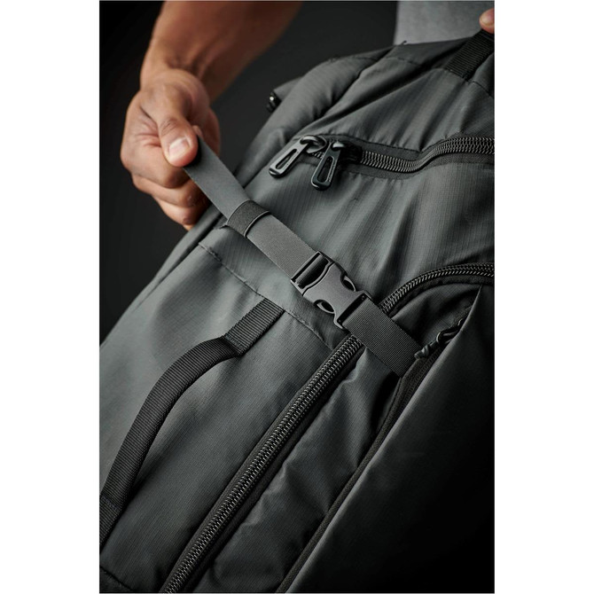 A grey duffle bag featuring zippers and a side strap adjustment, held by a person's hand for demonstration.