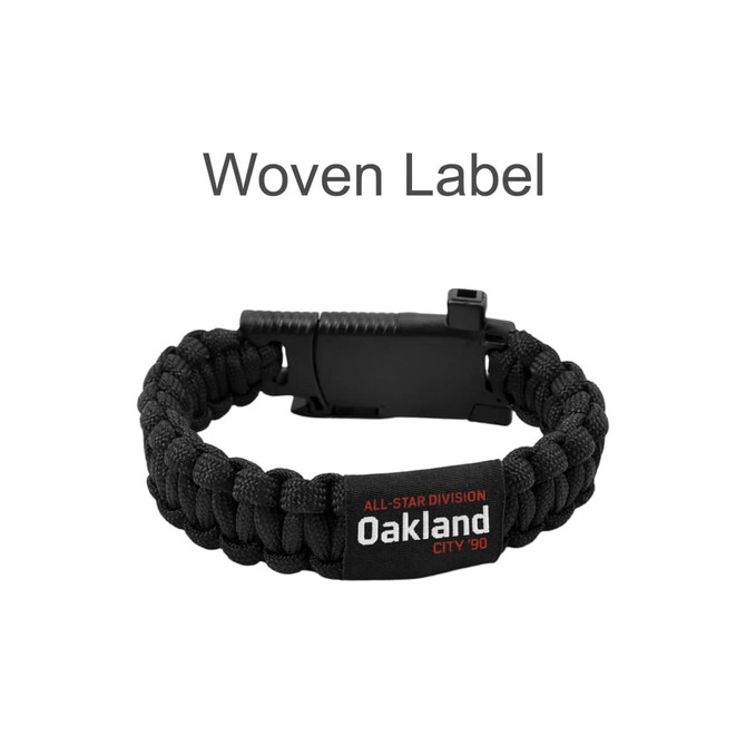 A black woven survival bracelet featuring a clip closure and an attached label.