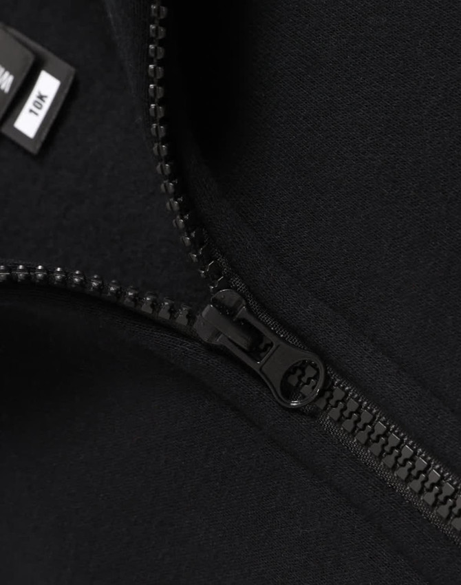 A close-up of a black fleece sweat with a half zip collar, featuring a smooth zipper and soft fabric texture.