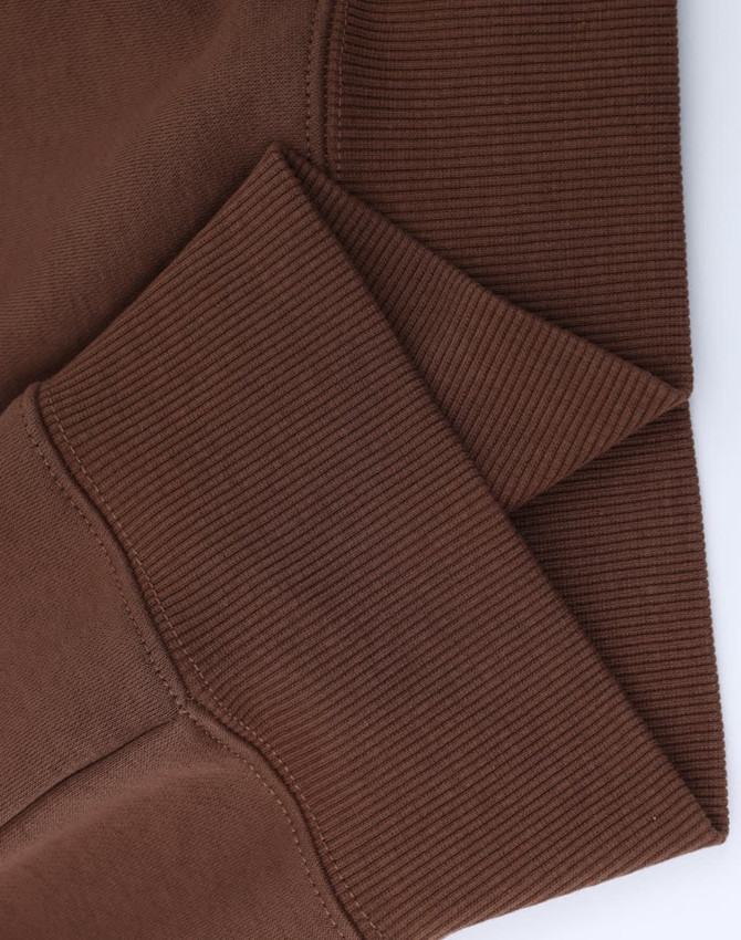 A close-up of the cuff detail on a brown unisex premium fleece oversized hoodie. The fabric is soft and ribbed.