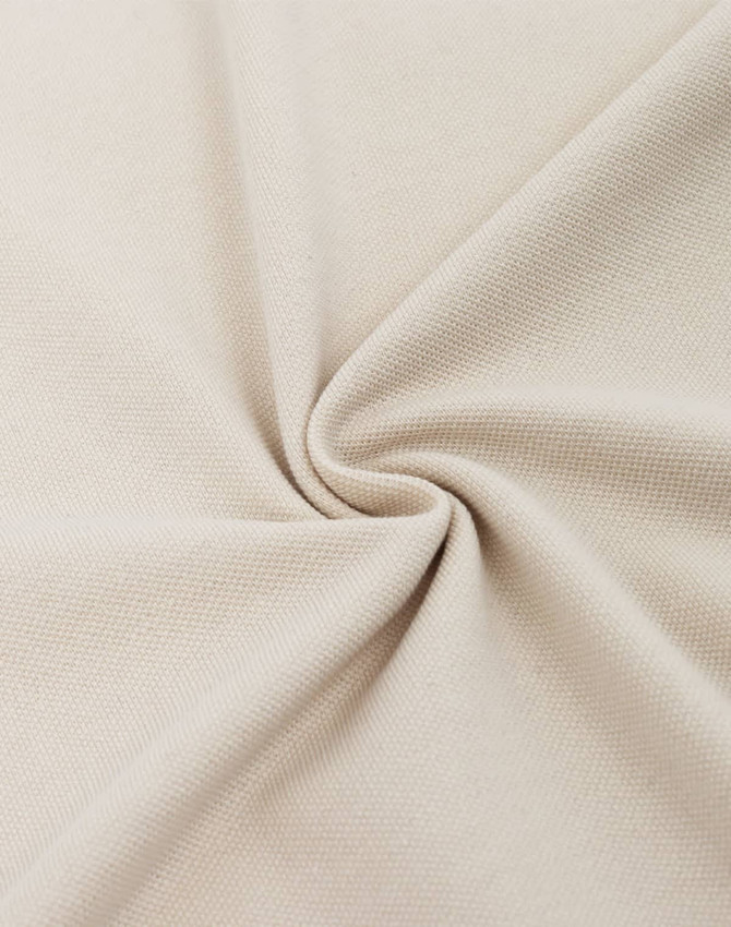 A close-up of beige cotton/polyester pique fabric, showcasing its texture and weave.