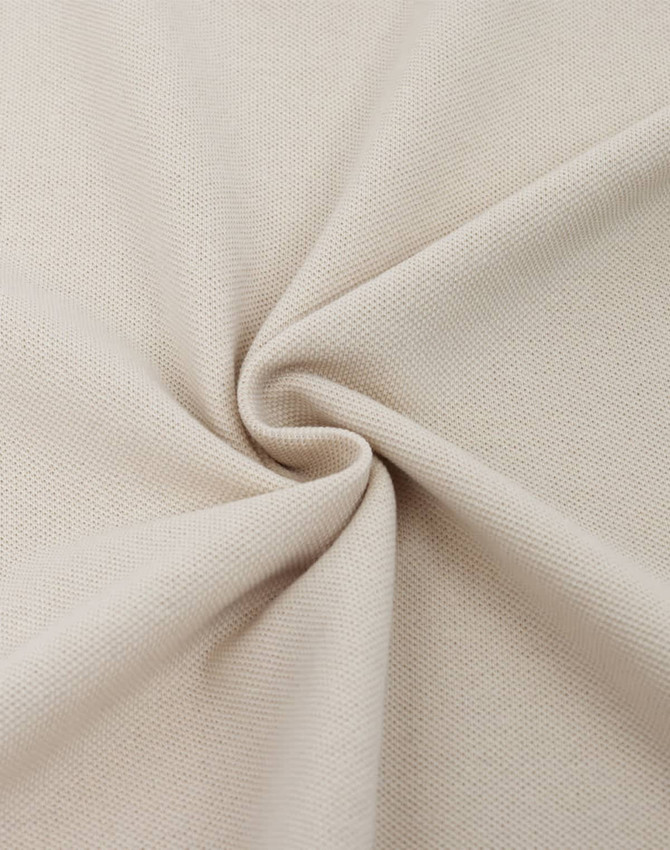 A close-up of light beige fabric, showcasing a textured cotton/poly pique weave. The fabric is folded in a spiral pattern.