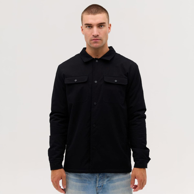 A black Studio Canvas Jacket features a collared design and front pockets, worn by a model against a plain background.