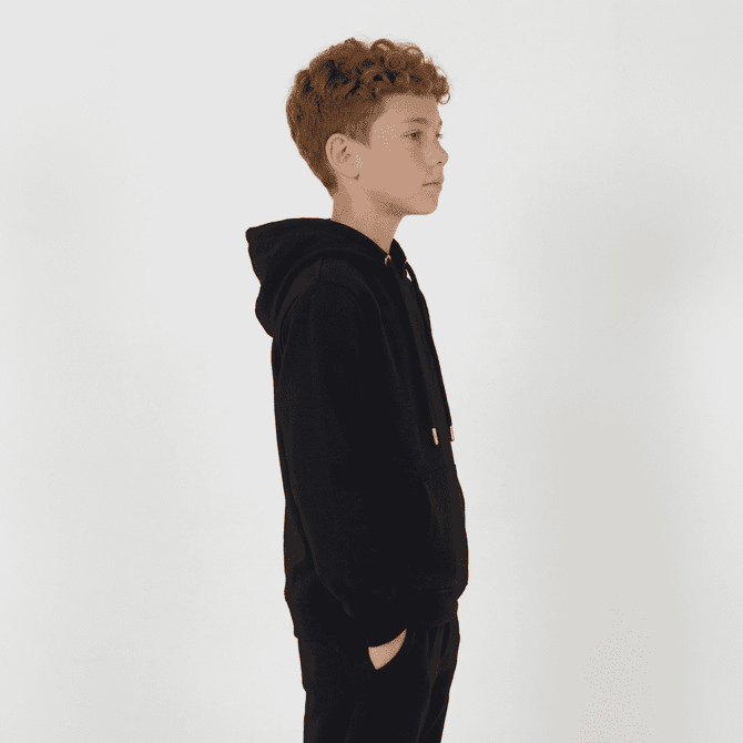 A black youth hoodie is displayed, featuring a hood and a kangaroo pocket. The model is a child with curly hair.
