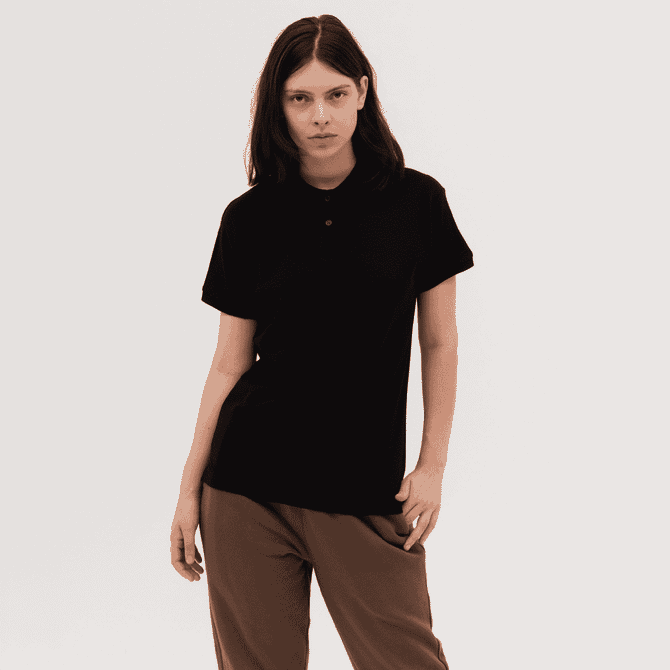 A black women's polo shirt displayed on a model, featuring a collar and short sleeves. The shirt has a branding logo.