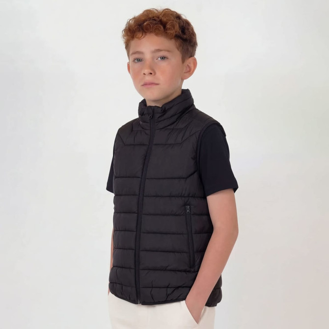 A black puffer vest for youth, featuring a zip closure and side pockets, worn over a black top.