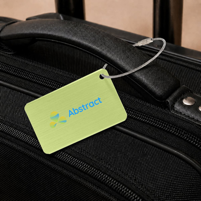 A brushed aluminium luggage tag in a rectangular shape, featuring a green background and a logo, attached to a black suitcase.