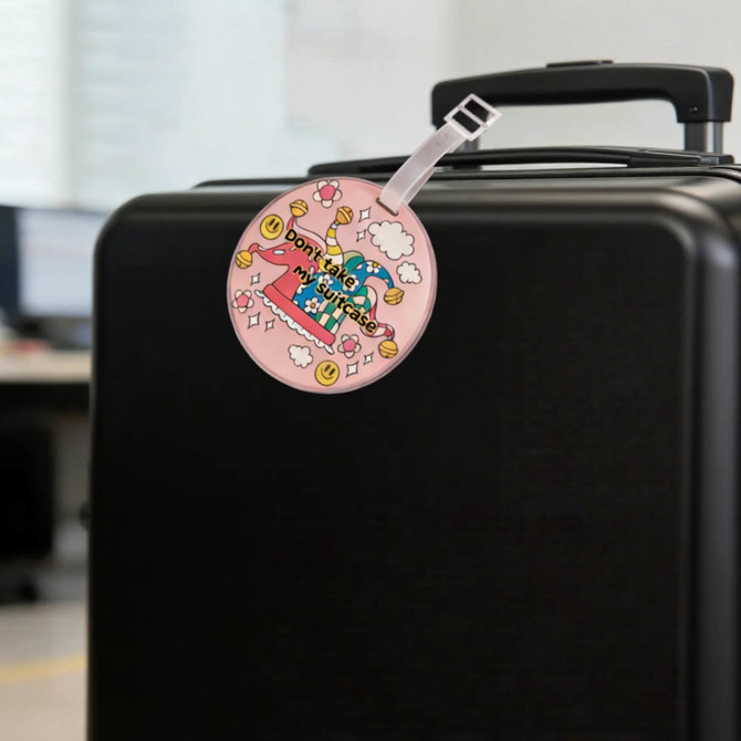 Acrylic luggage tag with a pink design, attached to a black suitcase handle, featuring a logo.