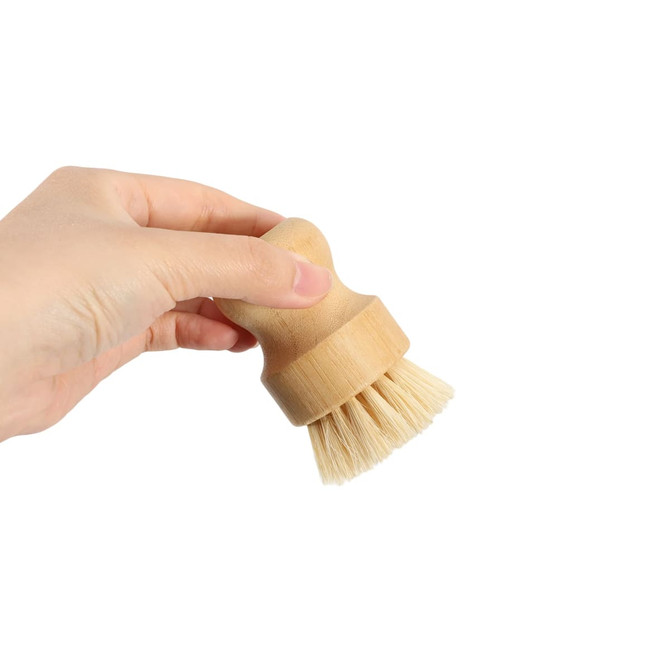 A bamboo kitchen dish brush with natural bristles, held in a hand. The handle features a light wood finish.