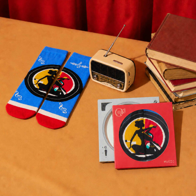 A red and blue pair of socks, a vintage radio, and two CDs in decorative cases on a table with books.