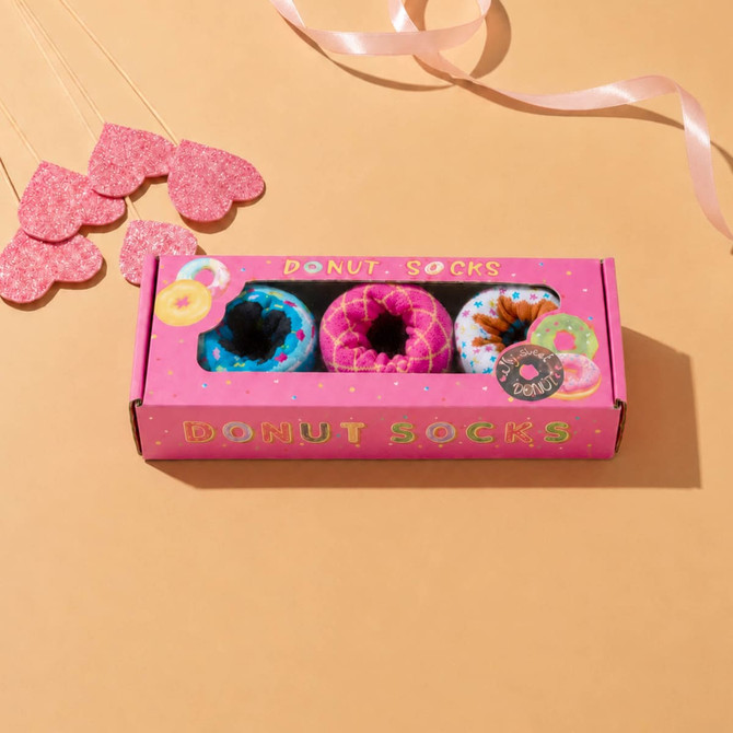 A pink gift box with a rectangular window displays brightly coloured donut-shaped socks inside.