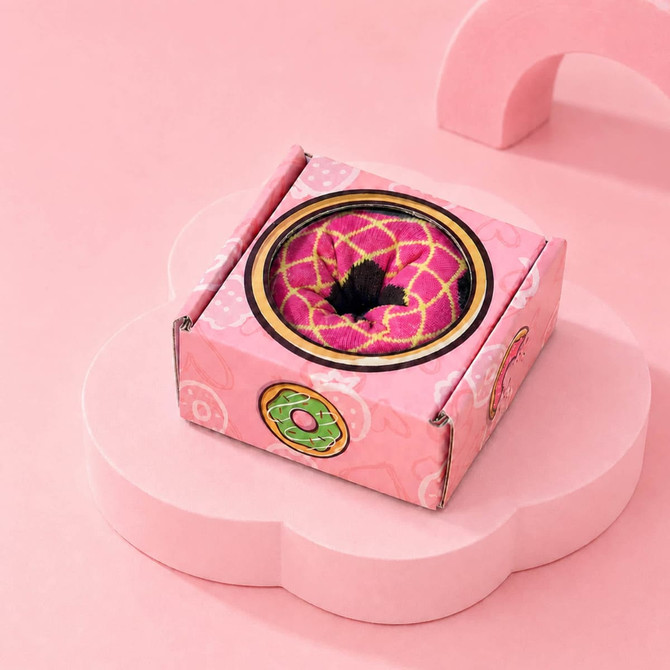 A small pink gift box with a round window, featuring a decorative design and a dark item visible inside.
