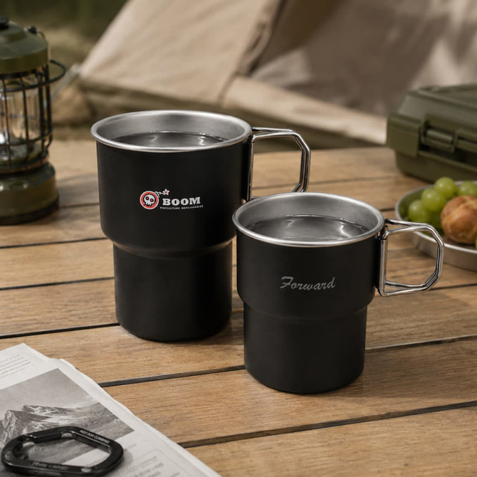 A set of two black stainless steel camping mugs with handles, featuring a logo on one mug.