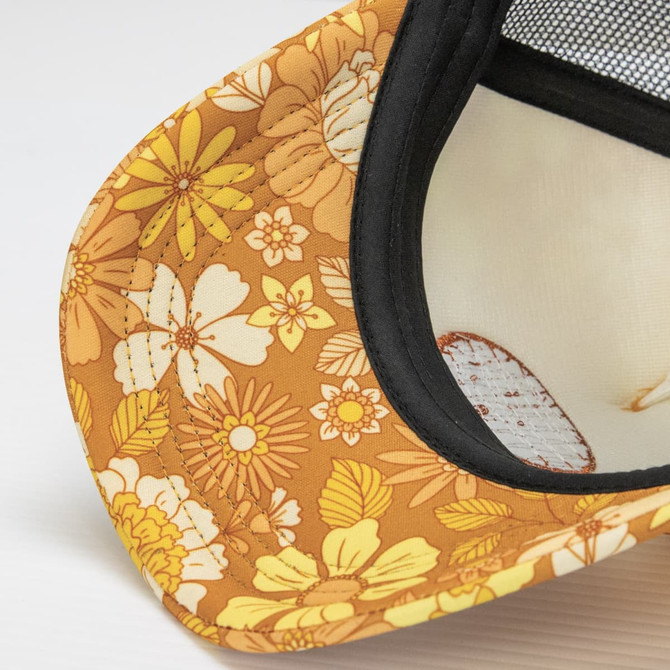 A trucker cap in warm yellow with a floral pattern and a black mesh backing. It includes a logo.