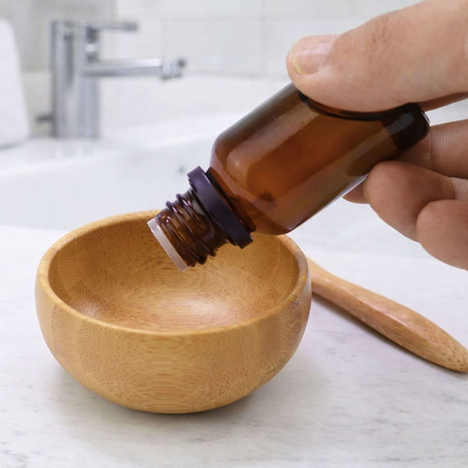 A bamboo bowl set with a wooden spoon and an amber glass bottle above it, showcasing a natural aesthetic.