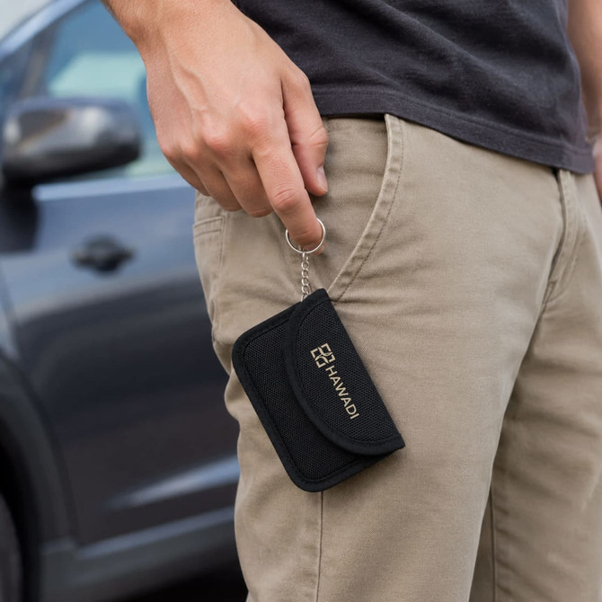A black RFID blocking key pouch held by a person while standing next to a car. It has a keyring attachment.