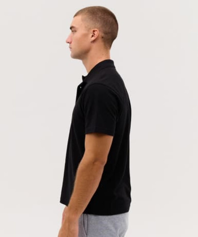 A black polo shirt displayed on a model in profile. The shirt features a collar and short sleeves.