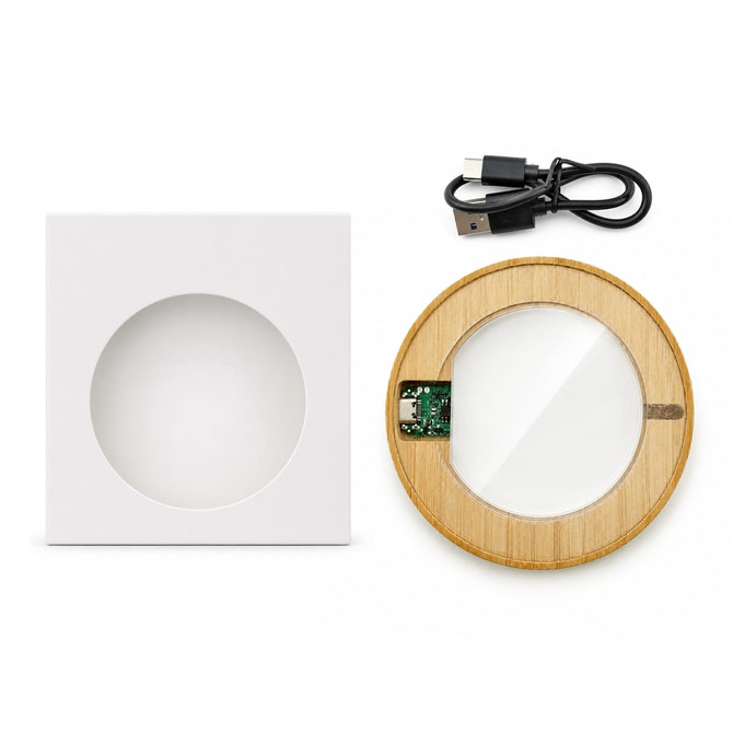 A circular bamboo wireless charger in a white square box, with a USB charging cable included.