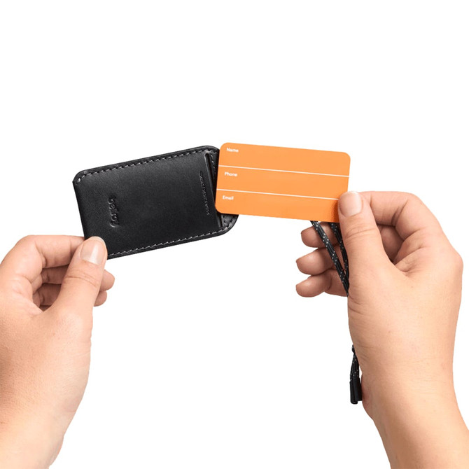 A black luggage tag is held in hands, revealing an orange identification card with spaces for personal details.