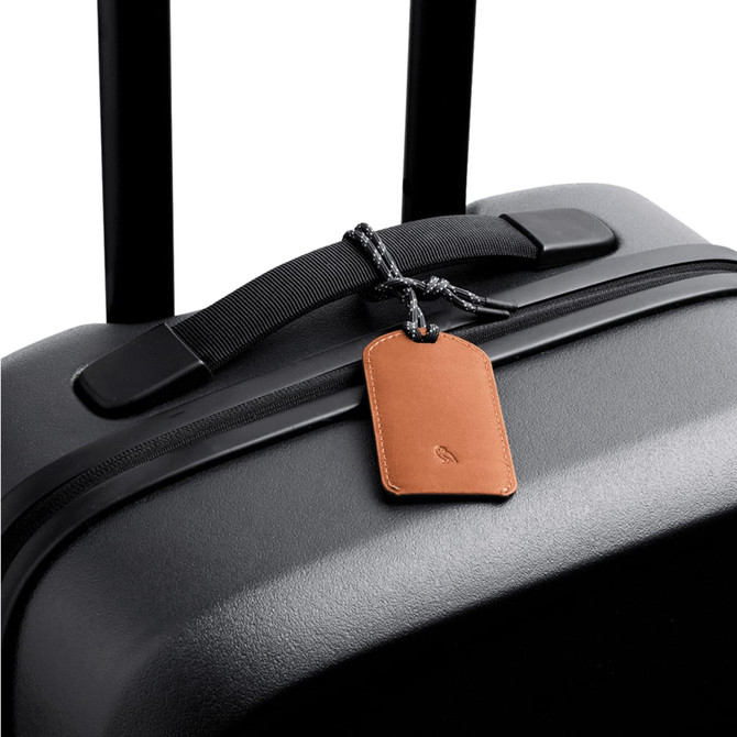 A black suitcase with a brown leather luggage tag attached, featuring a braided string for fastening.
