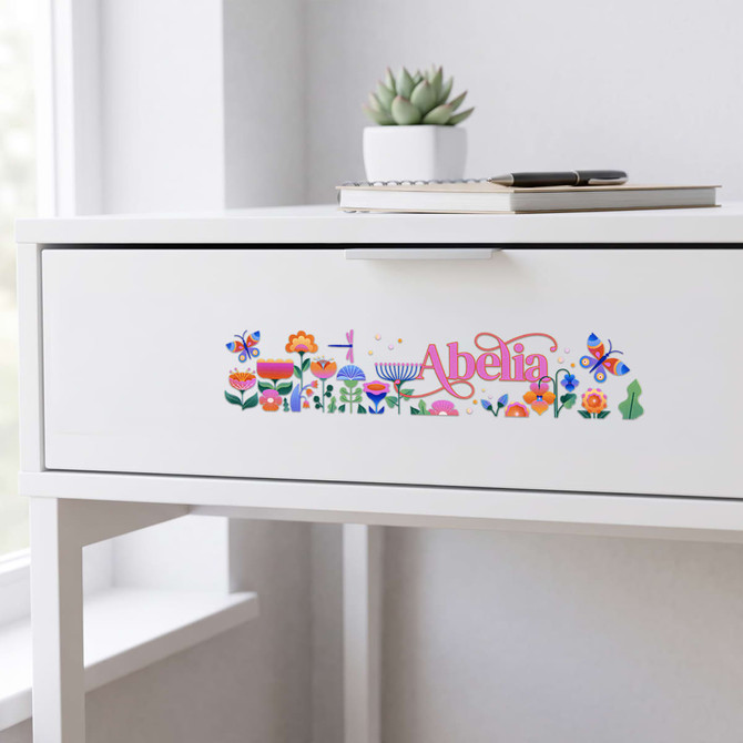 A drawer with a white finish featuring a colourful floral sticker with butterflies and the name "Abelia".