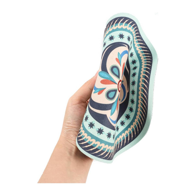 A patterned, heat-resistant trivet in shades of blue, green, and cream held in a hand. Features a decorative design and a logo.