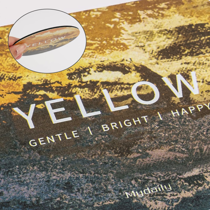 A round frosted metal coaster featuring a gradient of yellow and earthy tones, with a glossy surface and a small logo.