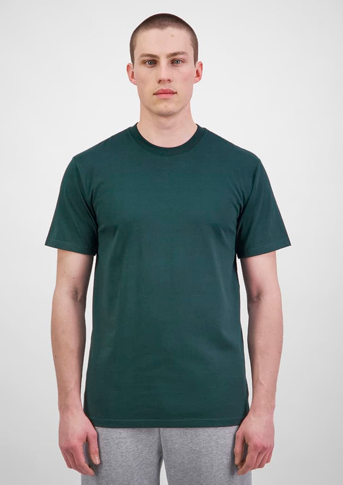 A plain green men's short sleeve tee, displayed on a model, paired with grey trousers. The shirt has a subtle logo.